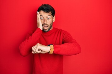 Poster - Handsome man with beard wearing casual red sweater looking at the watch time worried, afraid of getting late