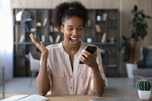 Overjoyed millennial African American woman look at cellphone screen celebrate triumph with lottery victory win. Excited young ethnic female feel euphoric with good online news on smartphone.