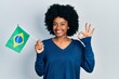 Young african american woman holding brazil flag doing ok sign with fingers, smiling friendly gesturing excellent symbol