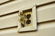 A close up image of an old yellow outdoor electrical receptor on a house.