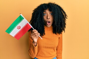 African american woman with afro hair holding kurdistan flag scared and amazed with open mouth for surprise, disbelief face