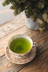 Green tea in a porcelain cup resting on an old wooden floor gives a warm feeling.