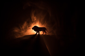 Wall Mural - A silhouette of lion miniature standing on wooden table. Creative decoration with colorful backlight with fog. Selective focus