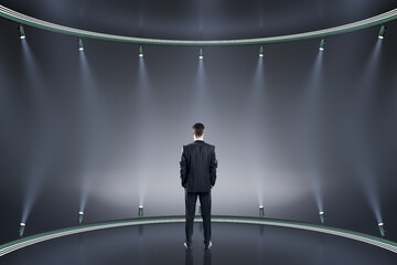 Back view of young businessman on creative stage background with illumination. Spotlight and fame concept.