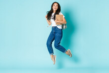 Fashion, Back To School And Lifestyle Concept. Cheerful Young Asian Girl, Korean Student Looking Upbeat, Holding Backpack And Notebooks, Jumping Upbeat Over Light Blue Background