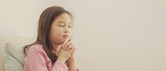 Wall Mural - Young mixed Asian girl praying with eyes closed, kid fellowship worshiping online at home, digital streaming church service, social distancing, peace and hope concept