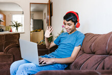 Latin Teenager With Headphones Making Video Call On Laptop At Home In Latin America