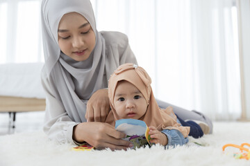 Mother and baby girl 6 months on the floor in the bedroom. Asian family in hijab clothing , single mom, motherhood, parenting, and child care