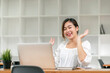 © NAMPIX - Young Asian woman using laptop video call talking with couple while working from home at living room.