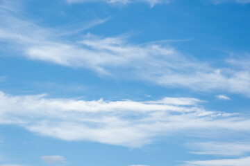 Real Soft Textured Feathery Clouds In Blue Sky Background. On a summer day, feathery fluffy clouds of various shapes and sizes slowly float across the light blue sky.