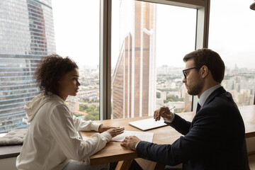 Canvas Print - African client applicant communicates with employer advisor during formal meeting in office boardroom, city with modern skyscrapers view through panoramic window. Negotiations, job interview concept