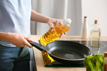 Young Woman Pouring Oil Into Frying Pan In Kitchen