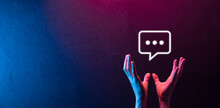 Hand On Neon Background Holding A Message Icon, Bubble Talk Notification Sign In His Hands. Chat Icon, Sms Icon, Comments Icon, Speech Bubbles