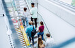 © Halfpoint - Rear view of university students walking up the stairs indoors, looking at camera and waving.