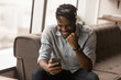 African hipster guy in dreadlocks hairstyle sit on sofa in modern office read sms on cell phone feels happy celebrate on-line auction betting victory. Gambling winner, good news, sales growth concept