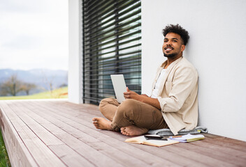 Wall Mural - Young man student with laptop sitting on patio outdoors at home, studying.