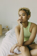 © shurkin_son - Young pretty Afro girl with natural beauty sitting on bed in morning in thoughtful pose with hand on her cheek dressed in bodysuit, looking straight to camera deep in thoughts, making plans for day