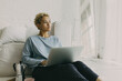© shurkin_son - Picture of modern female writer sitting on floor in thoughtful pose at her cosy light minimalistic apartment with laptop on knees dressed in home clothes coffeepot and cup on tray near her