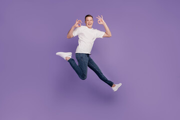 Wall Mural - Portrait of crazy promoter guy jump run hands show okey on purple background