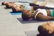 © Studio Romantic - Women in sports bra activewear lying down on floor in Shavasana, Mrtasana or Corpse Pose finishing group yoga session or enjoying restorative nidra sleep at gym, recreation center or fitness studio