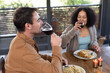 © Wavebreak Media - Happy diverse couple in living room sitting at table eating dinner together and drinking wine