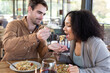 © Wavebreak Media - Happy diverse couple in living room sitting at table eating dinner together
