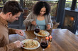 © Wavebreak Media - Happy diverse couple in living room sitting at table eating dinner together