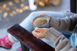 © Wavebreak Media - Happy mixed race woman in living room sitting by fireplace holding mug and drinking coffee