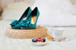 Morning still life. A small cake with fresh berries, a white porcelain teacup with cookies on a saucer and elegant turquoise-colored shoes with heels in the background in a blur.