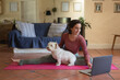 © Wavebreak Media - Smiling caucasian woman in living room with her pet dog, practicing yoga, using laptop