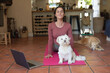 © Wavebreak Media - Smiling caucasian woman in living room with her pet dogs, practicing yoga, using laptop