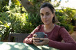 © Wavebreak Media - Portrait of smiling caucasian woman in garden, sitting at table drinking coffee