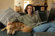 © Wavebreak Media - Portrait of smiling caucasian woman in living room, sitting on sofa with her pet dog, using laptop