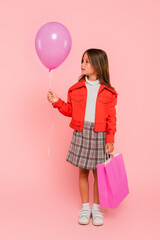 Wall Mural - girl in orange jacket and plaid skirt standing with balloon and shopping bag on pink