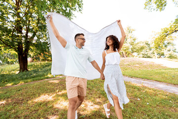 Poster - leisure, vacation and people concept - happy couple with picnic blanket walking at summer park