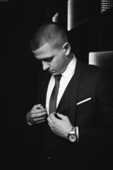 Wall Mural - Grayscale shot of a young man in a classic black suit on an illuminated background