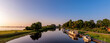 Sonnenaufgangs Panorama am See in Bederkesa. Brücke zwischen See und Kanal. Schiffe am Kanal, die von der Sonne angestrahlt werden. Sunrise at the lake in Bederkesa Germany. Panoramic view.