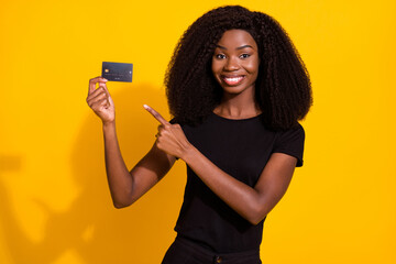 Sticker - Photo of attractive happy dark skin brunette haired woman point finger credit card smile isolated on yellow color background