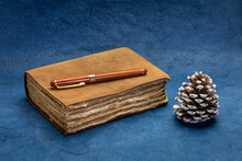 Antique Leather-bound Journal With Decked Edge Handmade Paper Pages With A Stylish Pen And A Decorative Pine Cone Against Blue Handmade Paper, Journaling Or Winter Holiday Greetings Concept