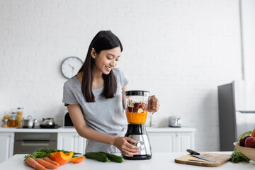 Wall Mural - happy asian woman preparing fresh smoothie for breakfast in kitchen.