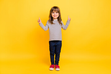 Wall Mural - Full body photo of cute little blond hair girl point empty space wear shirt jeans sneakers isolated on yellow backgound