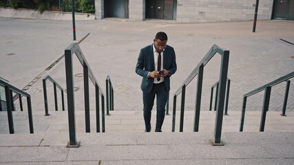 Modern lifestyle. Top view of focused african american businessman networking on smartphone and going upstairs