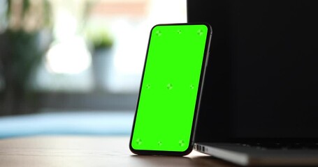 Wall Mural - a smartphone with a blank green screen with tags stands leaning against a laptop. slightly camera mo
