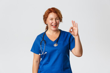 Medicine, healthcare and coronavirus concept. Confident professional doctor assure everything okay, cheerful middle-aged redhead nurse calm down patient, show ok gesture and winking encouraging