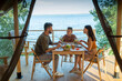 © pressmaster - Happy family of three having dinner by wooden table on terrace by seaside