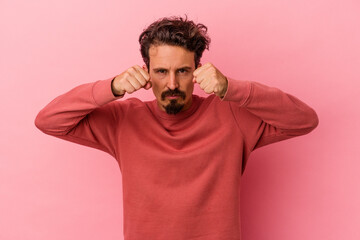 Young caucasian man isolated on pink background throwing a punch, anger, fighting due to an argument, boxing.