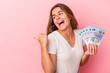 © Asier - Young caucasian woman holding bills isolated on pink background  points with thumb finger away, laughing and carefree.