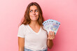 © Asier - Young caucasian woman holding bills isolated on pink background  confused, feels doubtful and unsure.