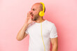 © Asier - Young caucasian bald man listening to music isolated on pink background  shouting and holding palm near opened mouth.