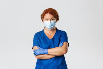 Medical workers, covid-19 pandemic, coronavirus concept. Professional cheerful female doctor, physician or nurse in scrubs, medical mask and gloves looking confident, cross arms chest, treat patients